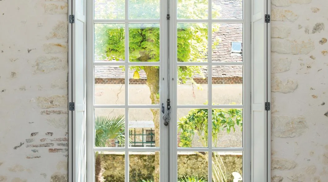 Porte-fenêtre bois blanche à petits bois ouverte dans un mur en pierre apparente à La Souterraine
