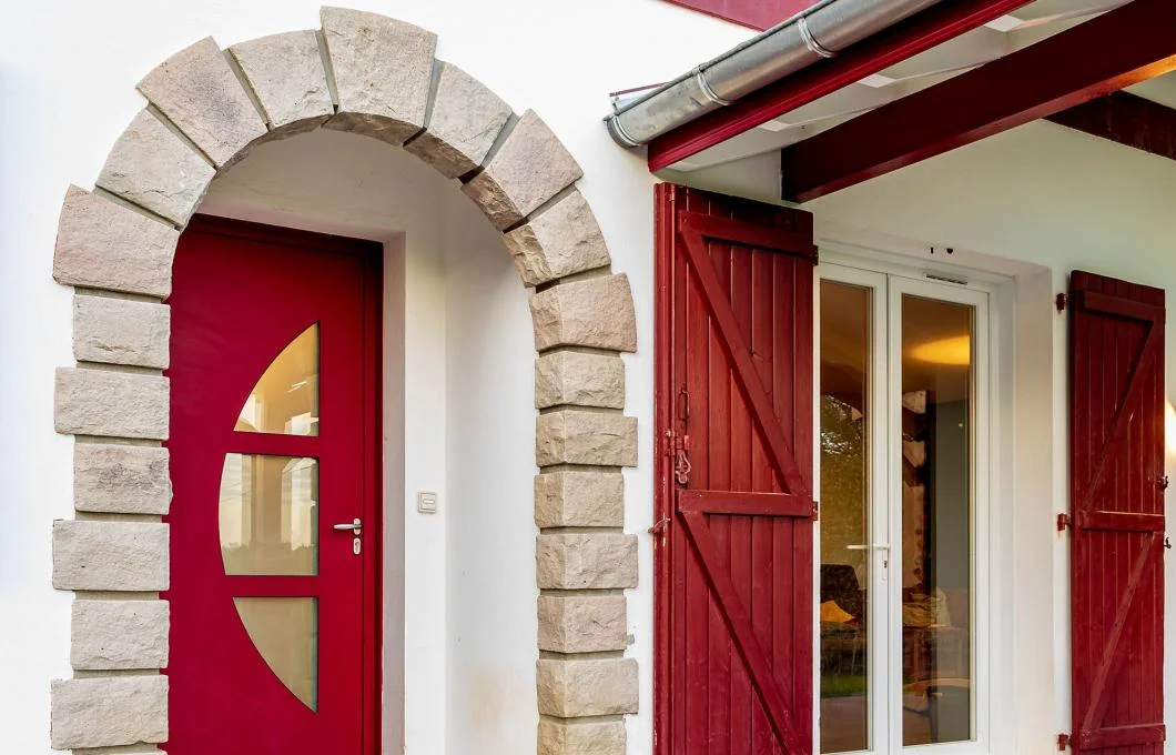 Porte-fenêtre PVC blanche et volets battants rouges sur une entrée en pierre de taille à La Souterraine