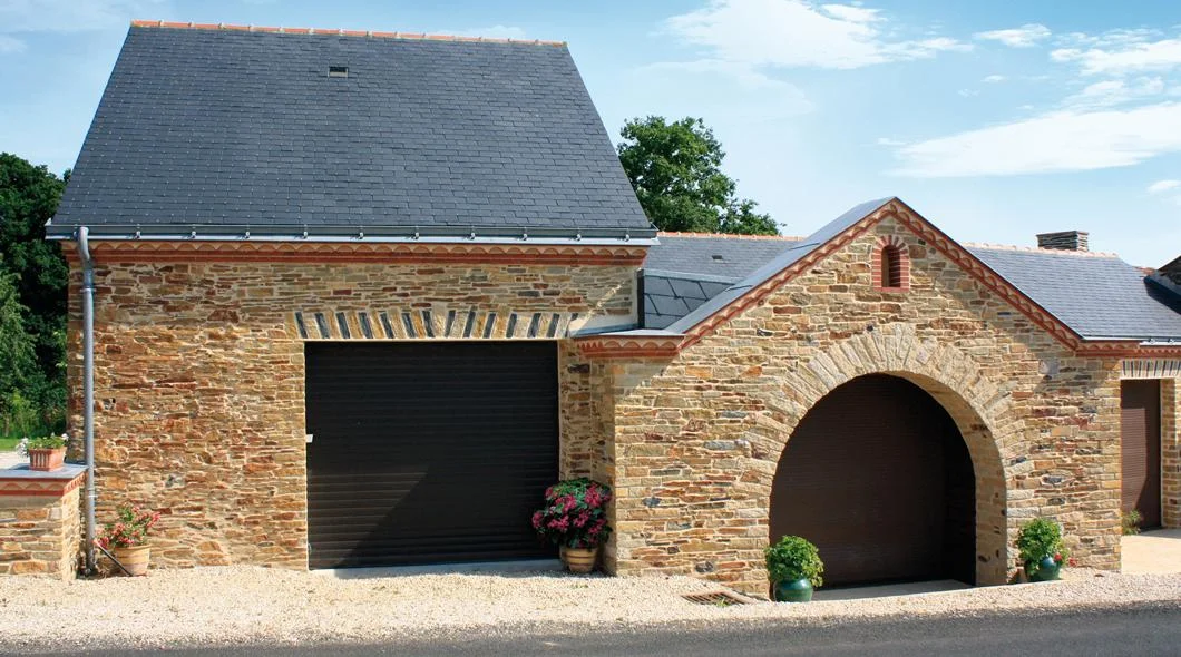 Porte de garage sectionnelle anthracite installée dans un garage en pierre à porche cintré, près de La Souterraine